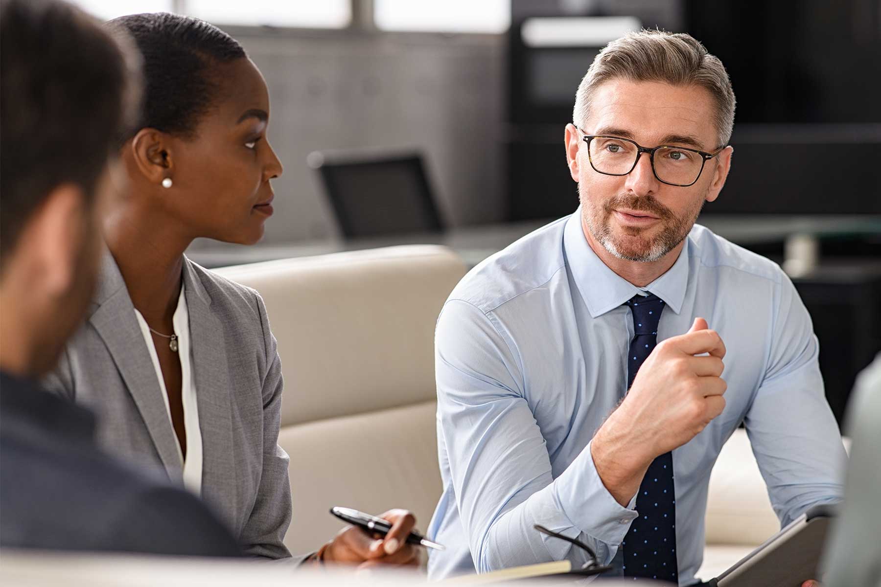 A man in glasses talks to two colleagues
